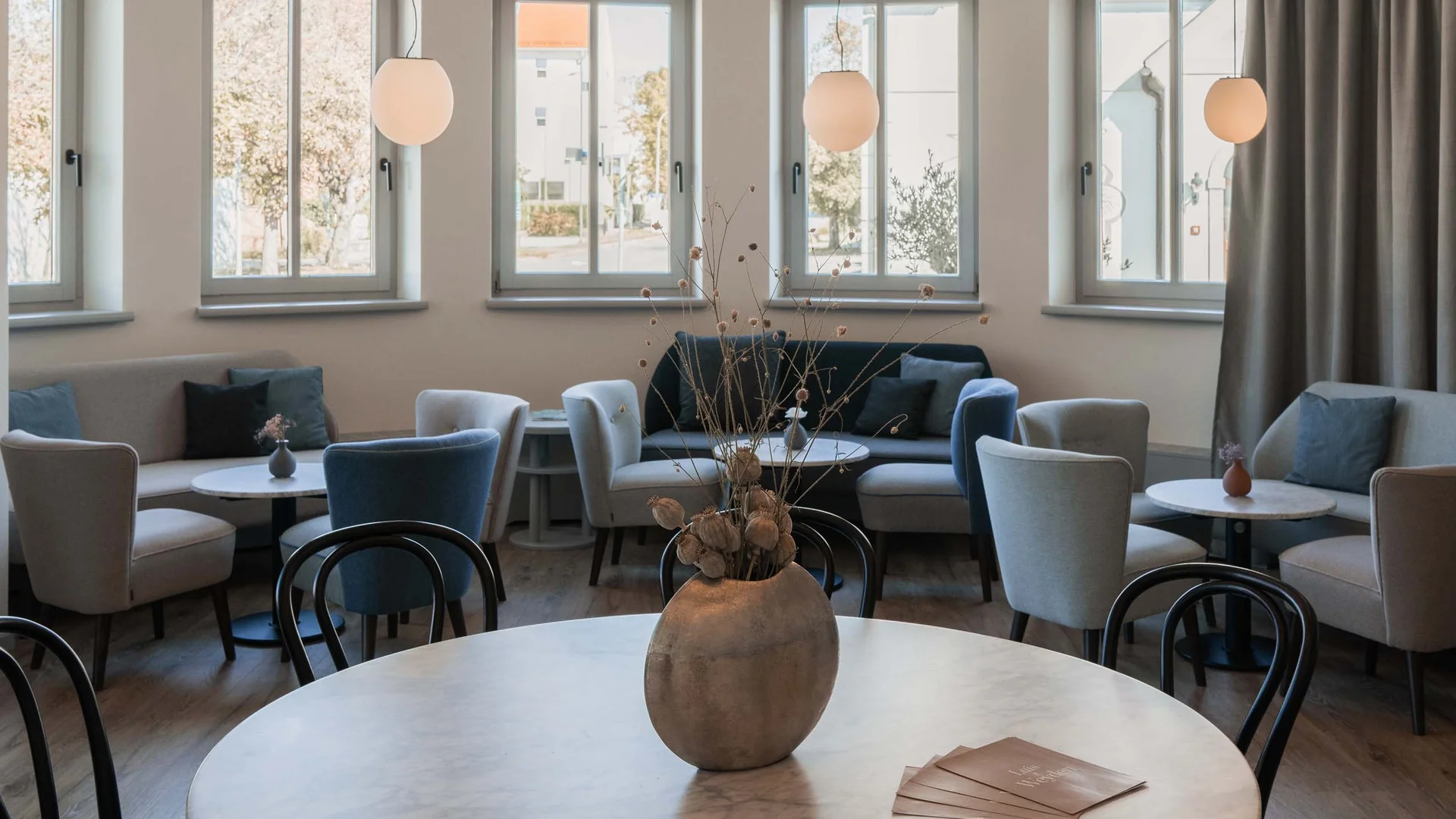 Modern eingerichteter Sitzbereich mit runden Tischen, Stühlen und großen Fenstern
