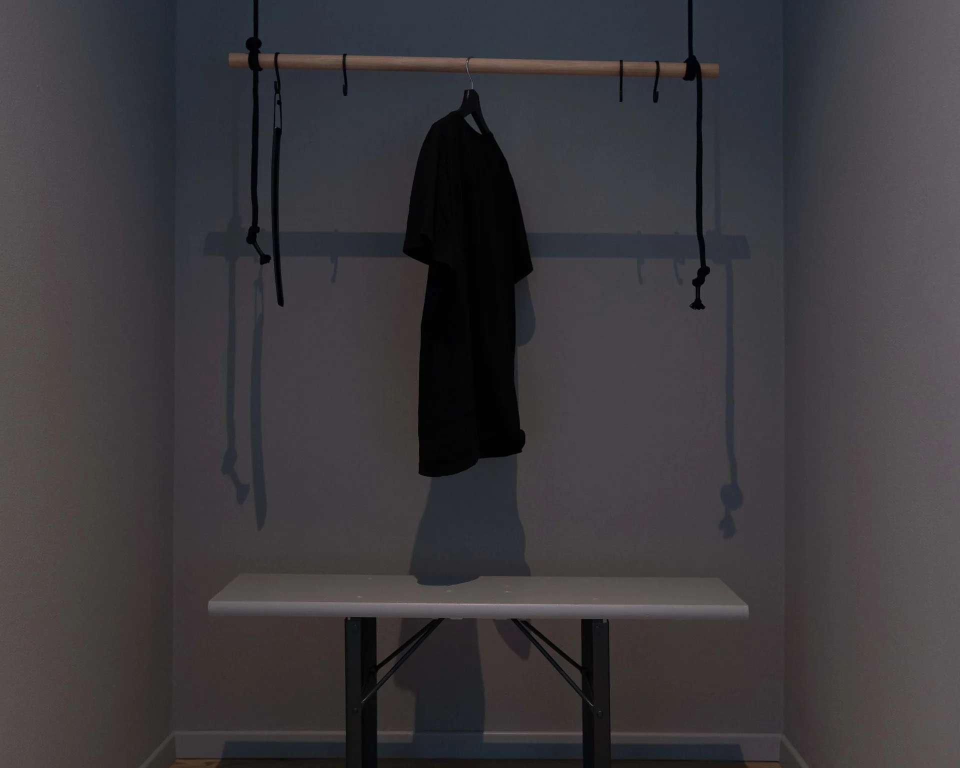 Schwarzes Kleidungsstück hängt an Holzstange über weißer Bank in dunklem Raum