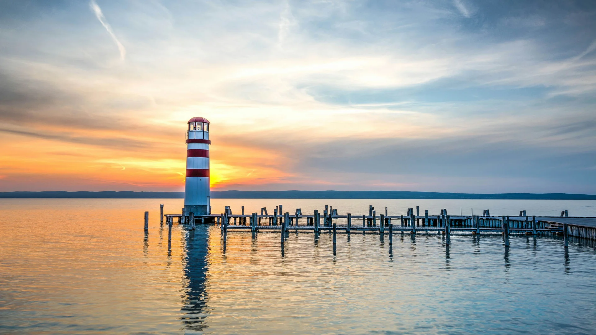 Neusiedler See Radweg: Übernachtung im Luis von Weyden Rot-weiß gestreifter Leuchtturm an einem Steg im ruhigen Wasser bei Sonnenuntergang