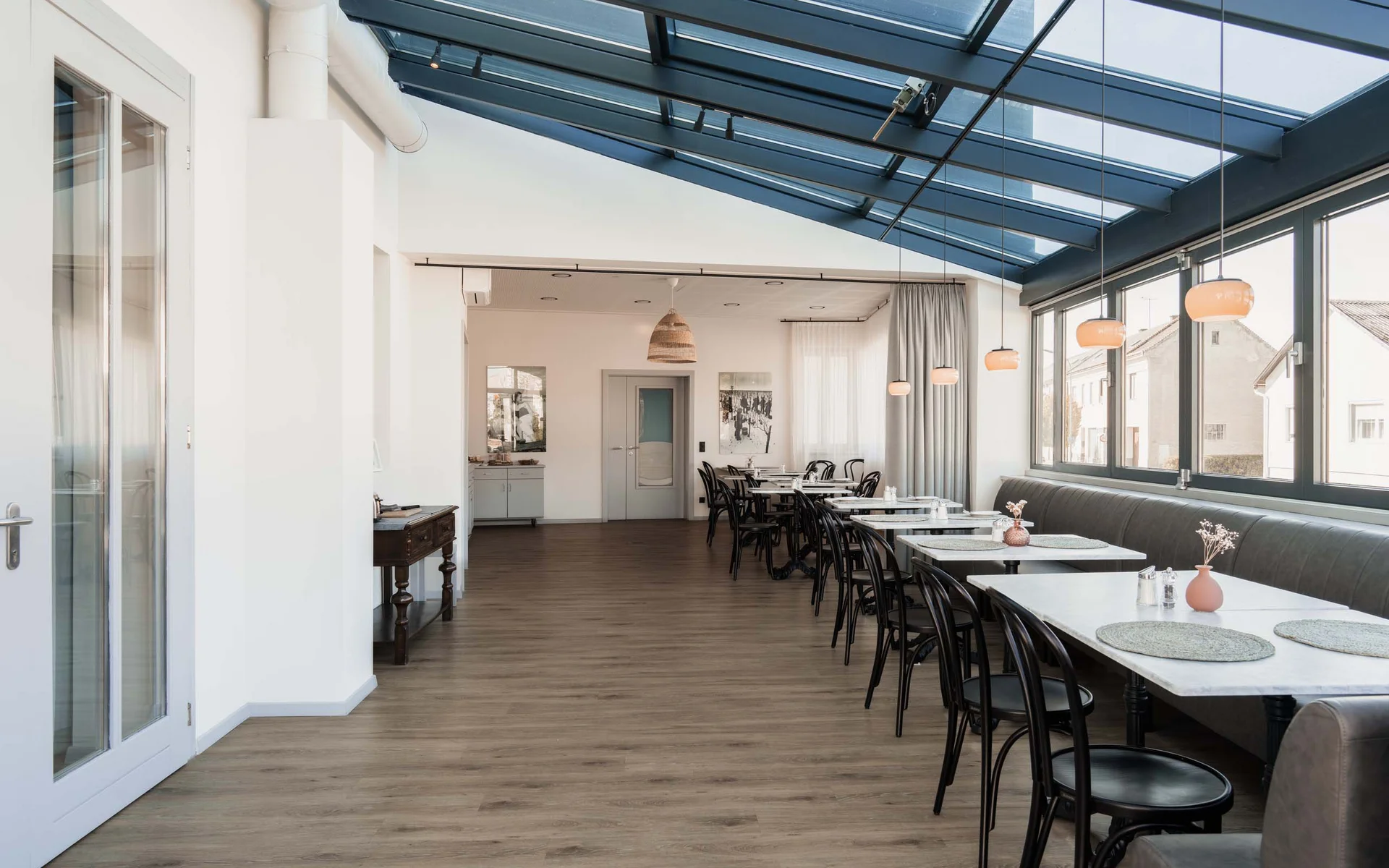 Moderner heller Speiseraum mit Glasdach und Tischen an Fenstern