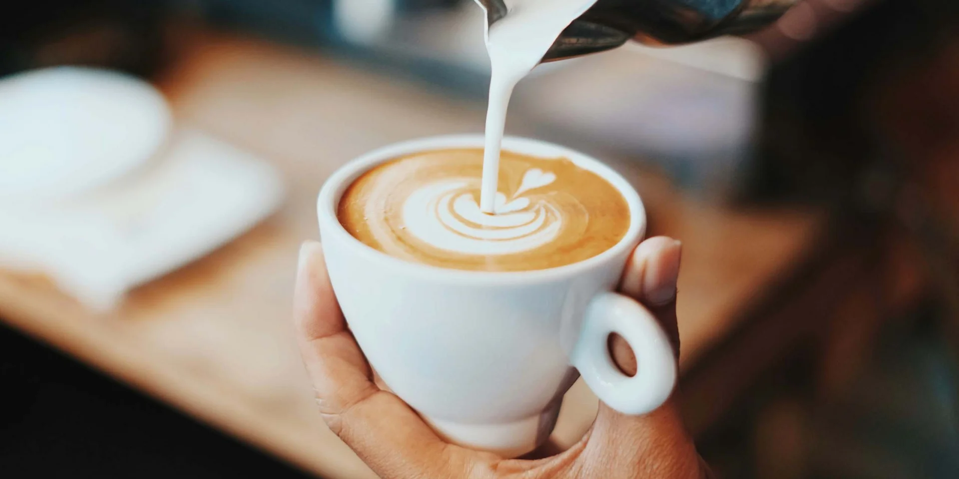 Hand hält Tasse Kaffee, Milch wird für Latte Art eingegossen