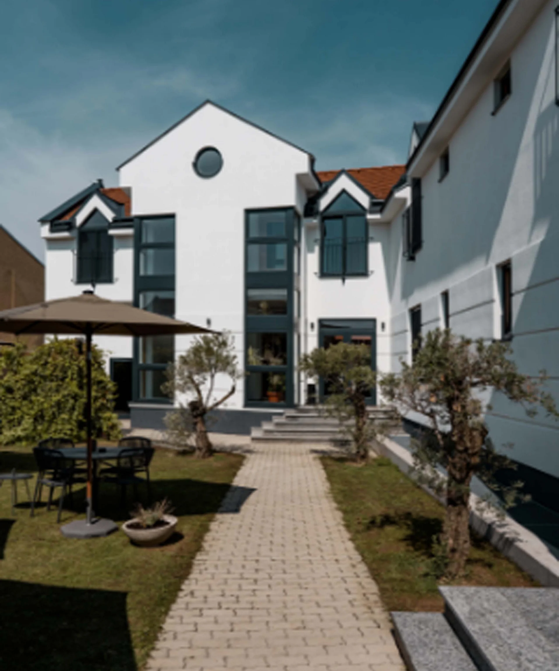 Weißes Mehrfamilienhaus mit Garten und Gartentisch mit Sonnenschirm