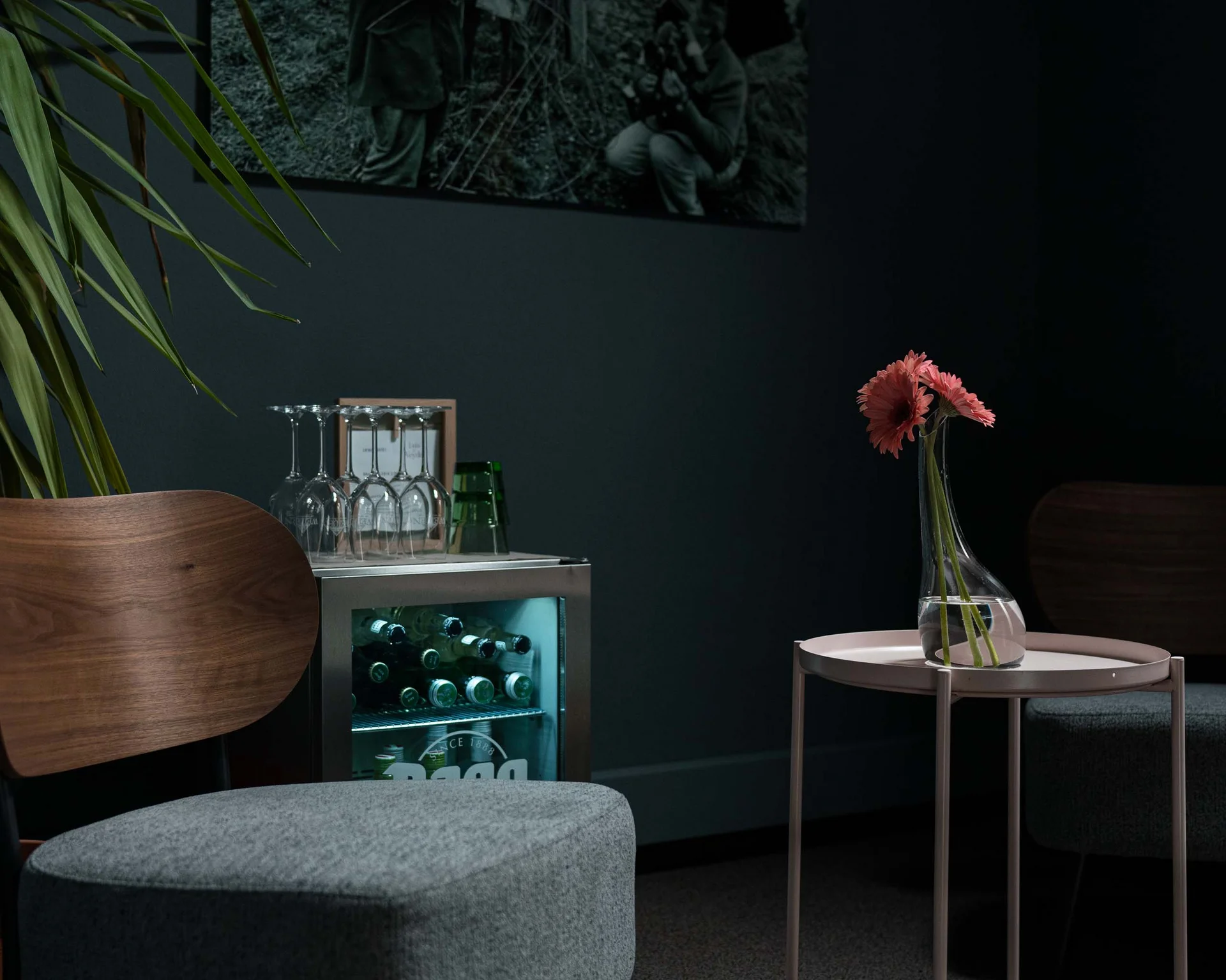 Dunkles Zimmer mit Sesseln, kleinem Tisch mit Blumen und Minibar