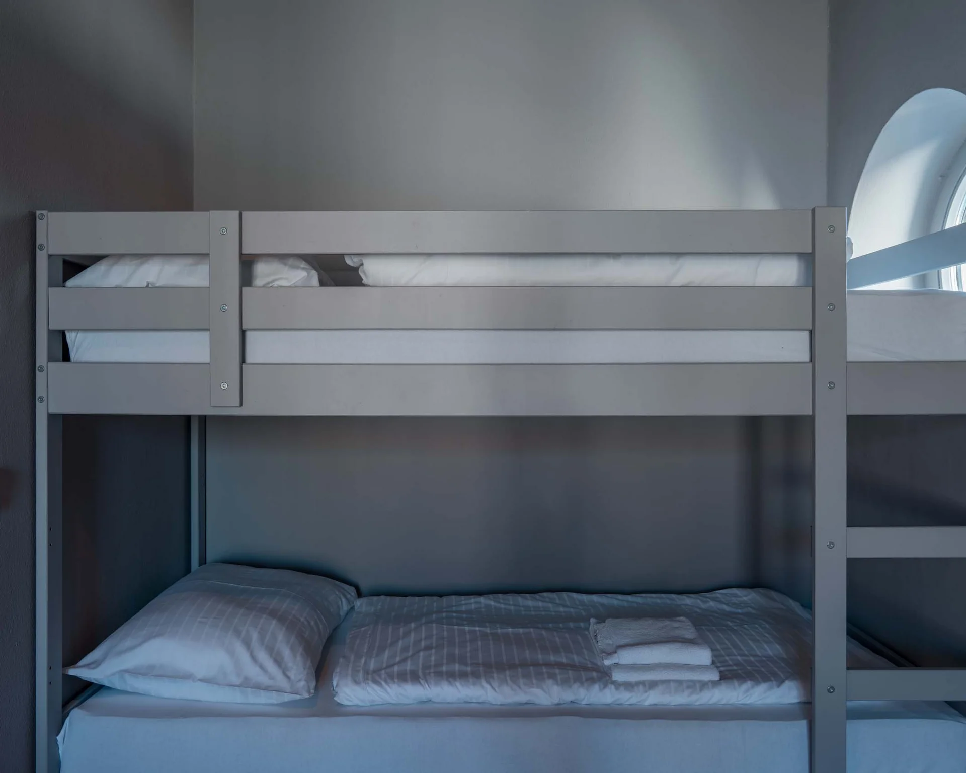 Graues Etagenbett in einem schlichten, grauen Zimmer mit rundem Fenster