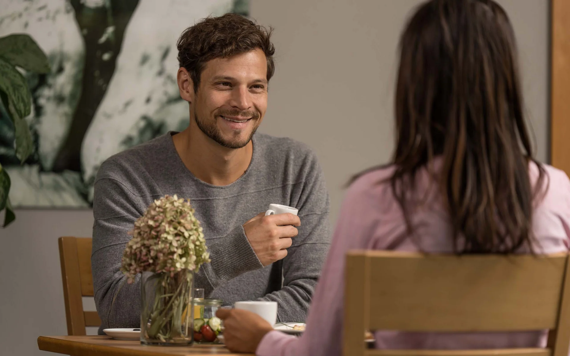 Mann und Frau sitzen am Tisch und trinken Kaffee, unterhalten sich lächelnd