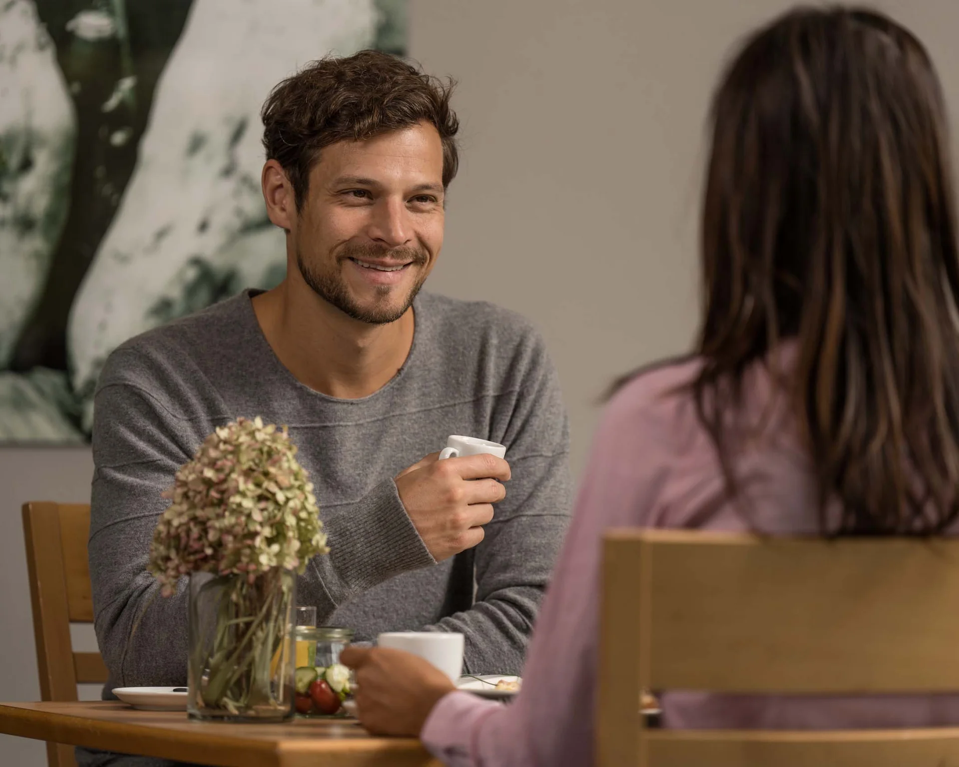 Mann und Frau sitzen am Tisch und trinken Kaffee, unterhalten sich lächelnd