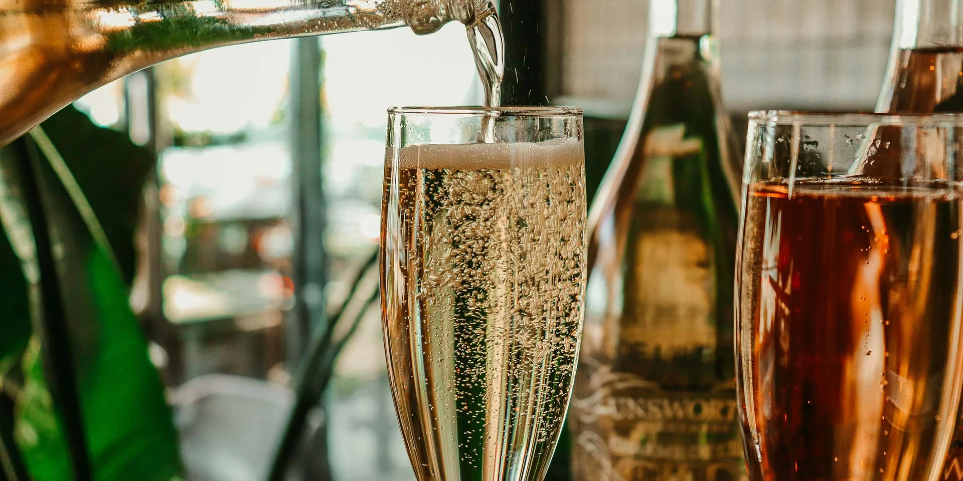 Sekt wird in ein Glas eingeschenkt, mit anderen Flaschen im Hintergrund