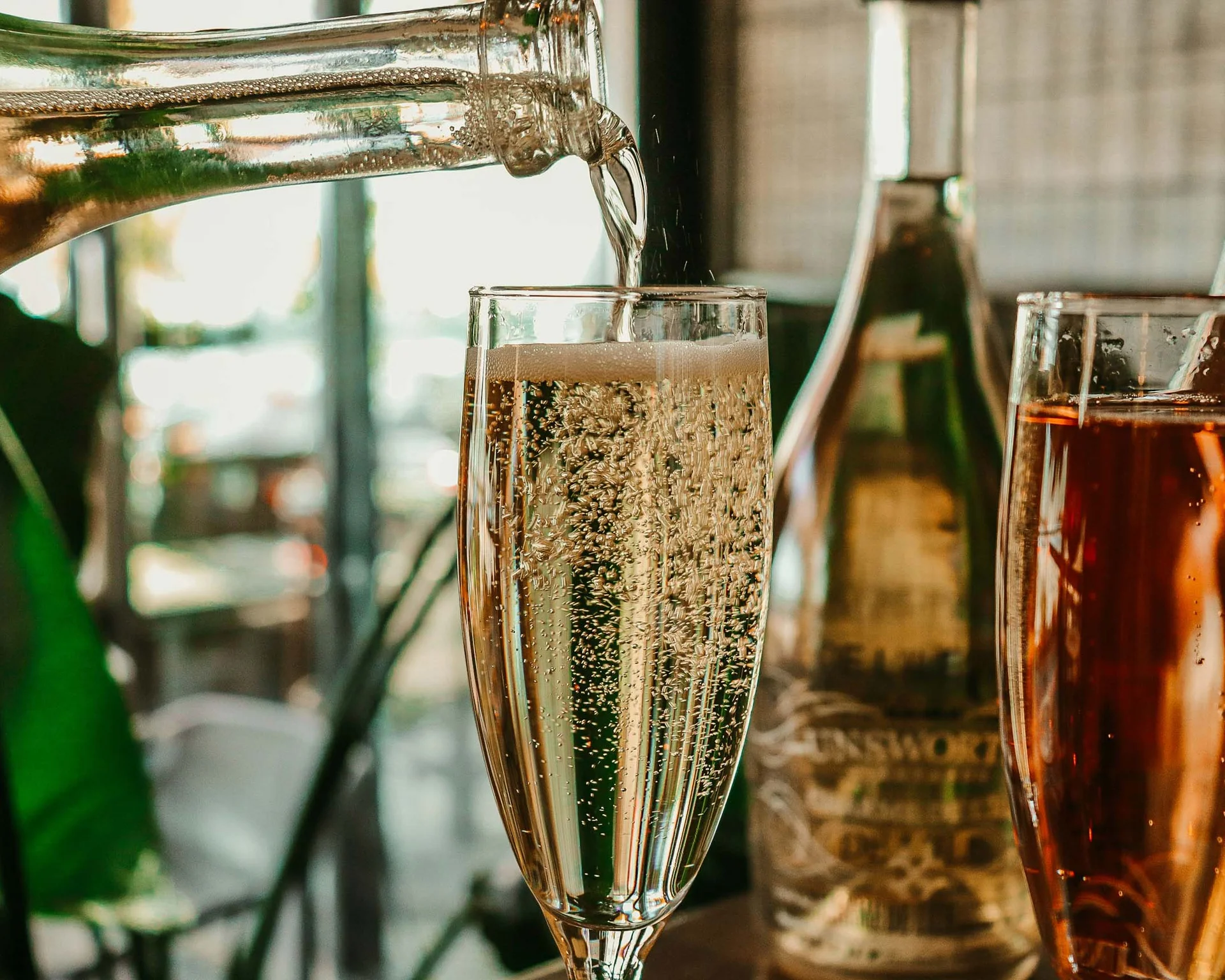 Sekt wird in ein Glas eingeschenkt, mit anderen Flaschen im Hintergrund