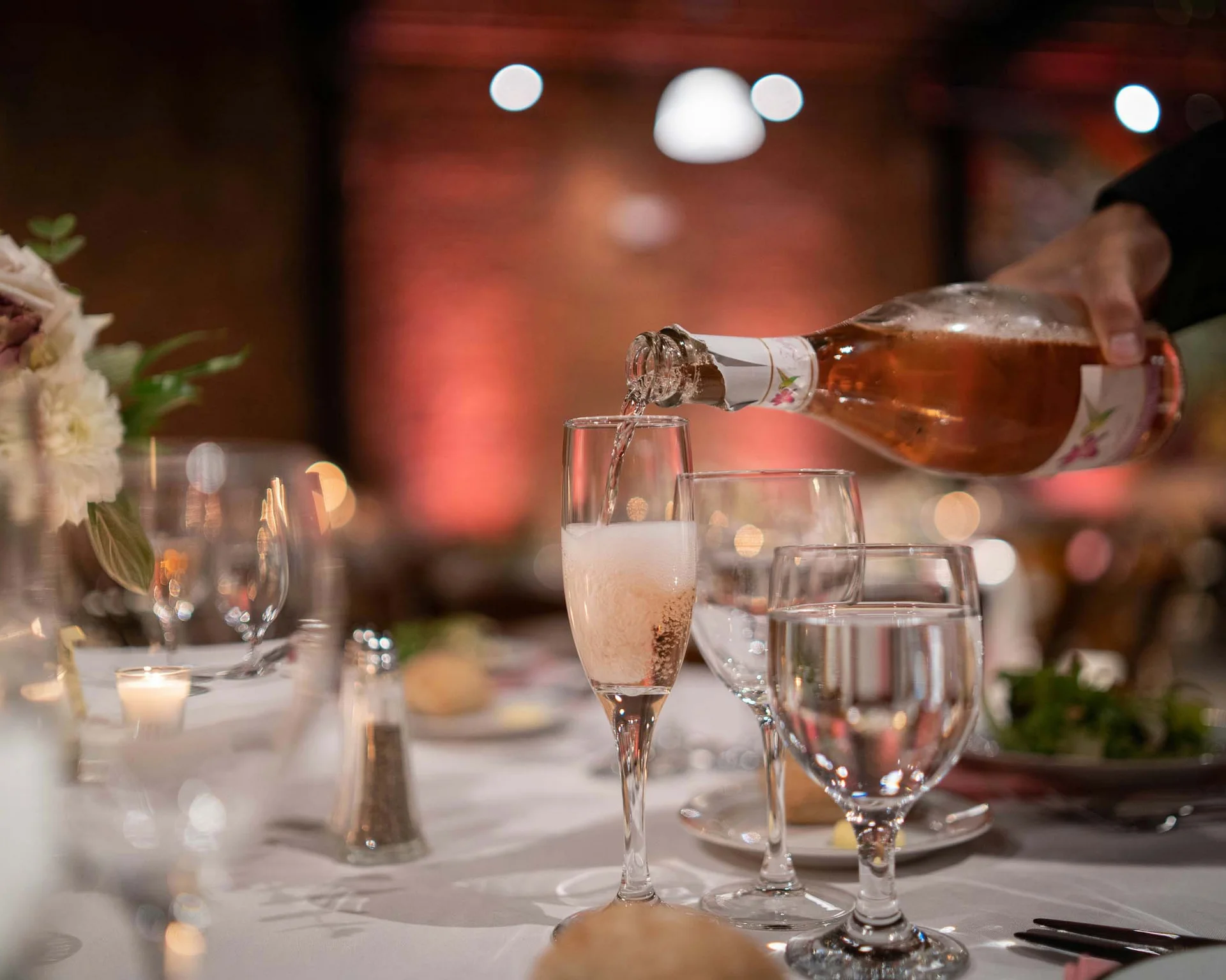 Sektflasche gießt in ein Sektglas bei einem festlich gedeckten Tisch