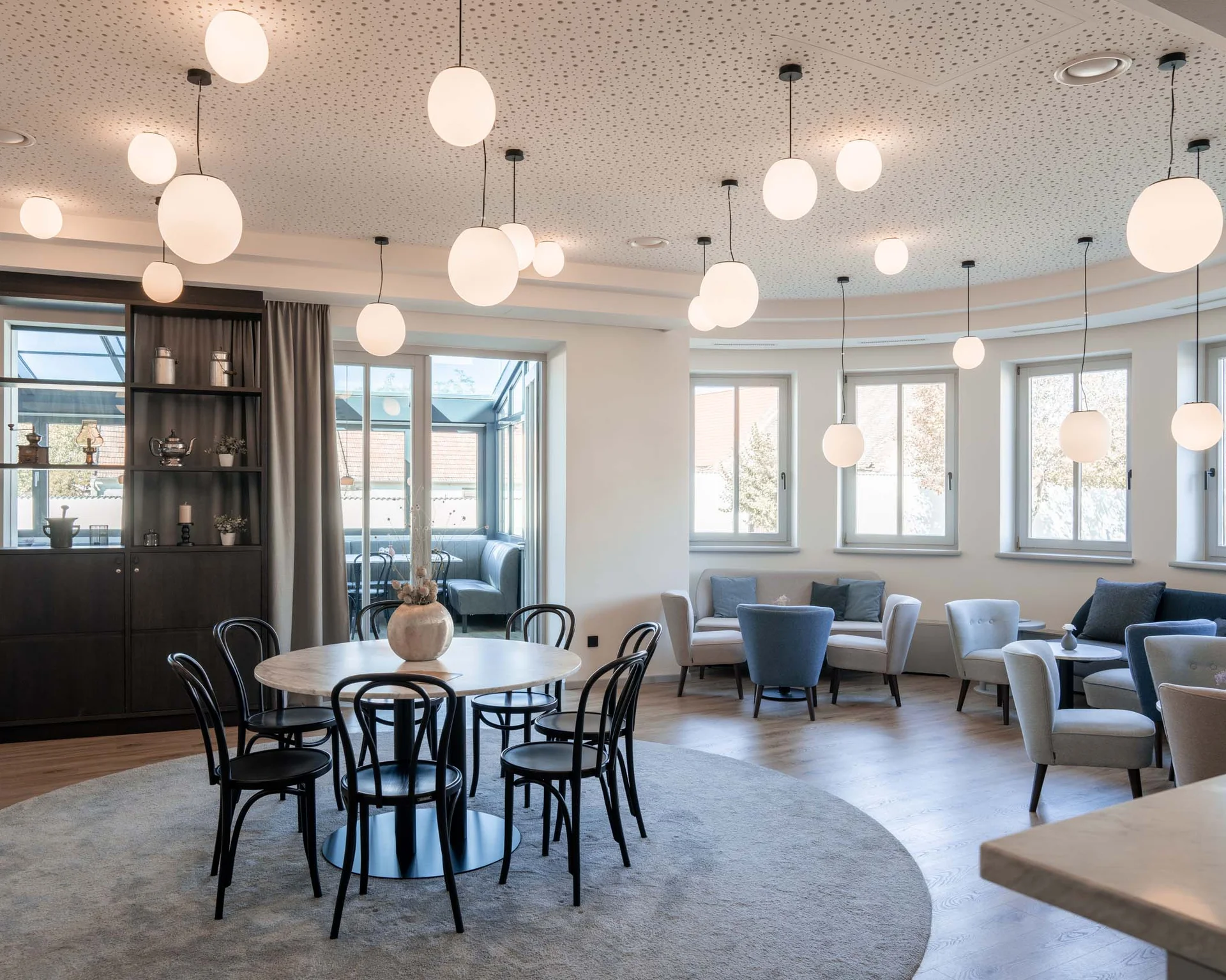 Heller moderner Aufenthaltsraum mit runden Tischen und ovalen Hängelampen