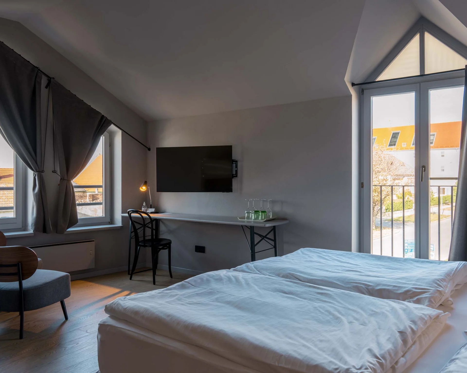 Helles Hotelzimmer mit Doppelbett, Schreibtisch, Stuhl und Balkonfenstern